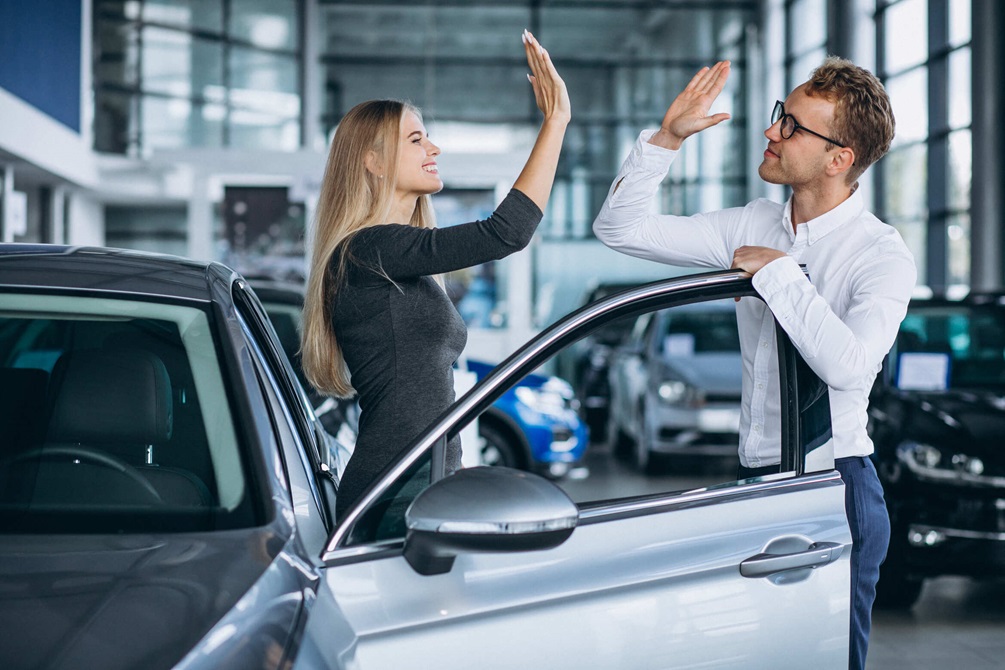 Salesperson and customer shaking hands in a car dealership showroom.